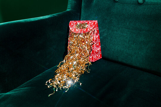gold tinsel overflowing from a red holiday bag on a green armchair