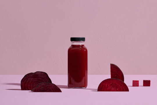Fresh beetroot juice in bottle with sliced beets on a pink background