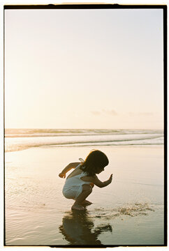 Child squatting to play in water at sunset beach