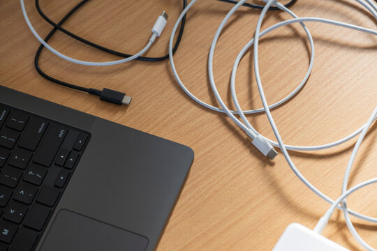 USB-C Cables Tangled Beside Laptop on Wooden Desk