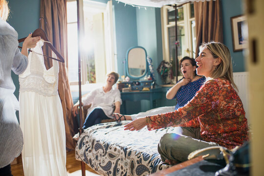 Women reacting with joy as a dress is shown in a bright bedroom