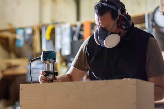 Carpenter Using Router Tool With Respirator in Woodworking Workshop