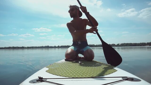 Surfer Kneeling On Stand Up Paddleboard Rowing In Calm River Water. Water Sports Recreation