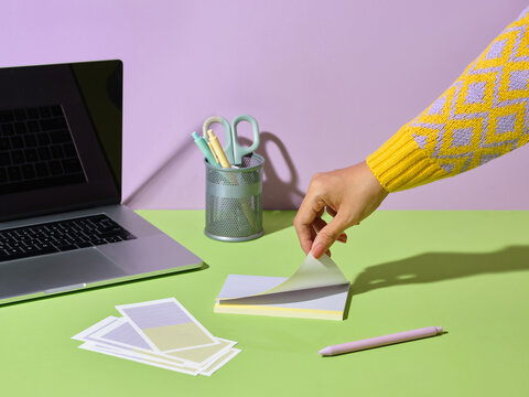 Woman's hand peeling a sticky note on a colorful desk with a laptop