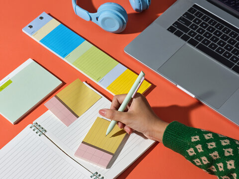 Woman writing on a notepad with a pen, laptop and headphones on a desk