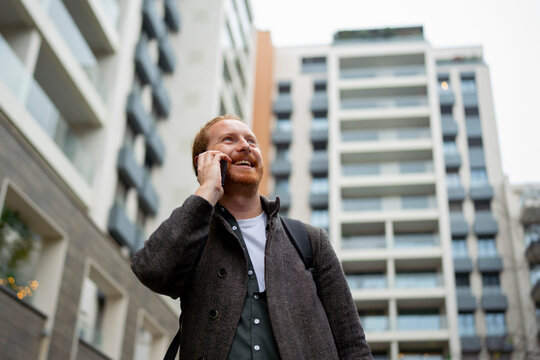 Person talks on phone in urban setting near modern buildings
