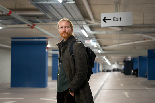 Man stands in empty parking garage near exit sign
