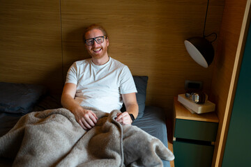 Smiling man sitting on bed in cozy room during morning hours
