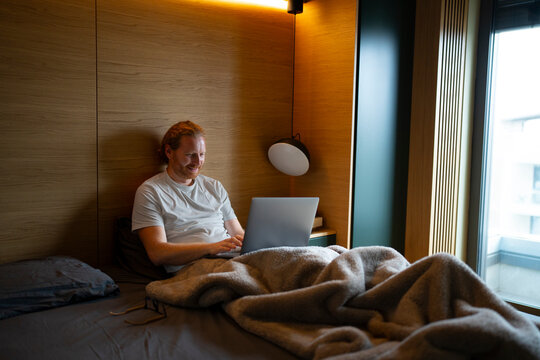 Man working on laptop in bed during evening hours
