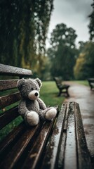 A solitary plush toy, a soft grey teddy bear, sits patiently on a wet wooden park bench during a gentle rain shower. The scene evokes profound feelings of nostalgia, melancholy, solitude, and quiet re