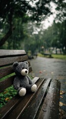 A solitary gray plush toy sits abandoned on a dark, rain-soaked wooden park bench, its presence evoking a profound sense of loneliness and melancholy. Gentle rain streaks are visible against the blurr