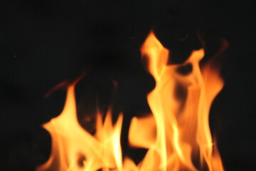 Vibrant orange fire flames flickering against a pitch black background. Abstract heat energy texture with soft blur and glowing sparks. Perfect for concepts of danger, warmth, energy, or industrial bu