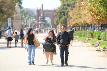 A man and two women are walking down a sidewalk in a city. The man is talking on his cell phone while the women are walking beside him. There are many other people walking around them