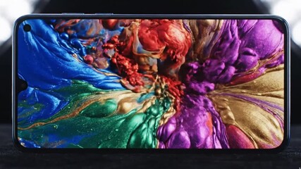 A modern smartphone displays a captivating and vibrant abstract liquid animation on its screen. Dynamic iridescent colors of blue, green, gold, red, and purple fluidly swirl, mix, and expand, creating