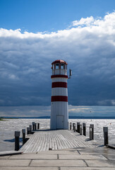 Red and white striped Podersdorf Lighthouse Austria standing on wooden pier under dramatic cloudy sky