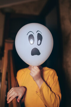 Child holding ghost balloon in front of face fooling around at Halloween
