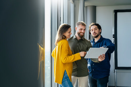 Smiling businessman discussing with colleagues over tablet PC in office