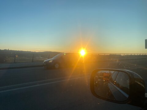 ief stehende Sonne blendet den Fahrer auf einer Stra&szlig;e w&auml;hrend der Fahrt. Das Motiv steht f&uuml;r Verkehr, Sonnenblendung, Sicherheit, Pendeln und Abendstimmung unterwegs.