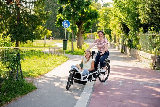 Friends riding cargo electro bike outdoors on urban cycle path