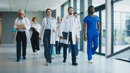 Medical staff walking through clinic hallway with focused expressions. Doctor checking time while colleague carrying folder. Professionals moving together and coordinating duties during busy shift.
