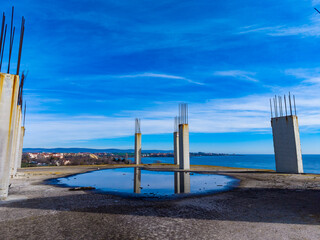 Construction site with concrete pillars and water reflection near the shore during daytime