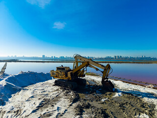 Construction equipment is operating near water with a city skyline in the background during clear weather