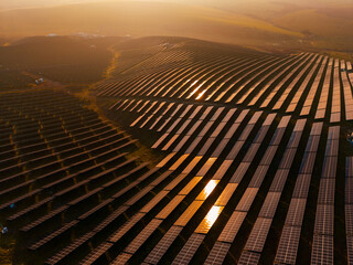 Power generation takes place at a solar energy farm during sunset with rows of solar panels...