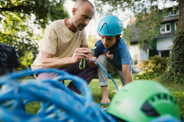 Father teaching son climbing rope techniques in summer garden