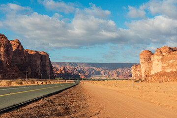 Desert road from Al Ula to Hegra in Saudi Arabia through red rock canyon with vast sky and rock formations under bright blue sky