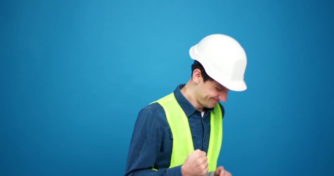 Positive, happy foreman wearing safety hard hat and green vest dancing isolated on blue background