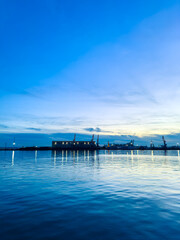 Fototapeta premium Sunset over the harbor with cranes and calm water at dusk near a shipping facility and a clear sky