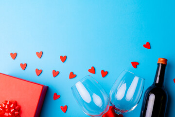 Heart shaped decoration with wineglasses and bottle by gift on blue background, copy space