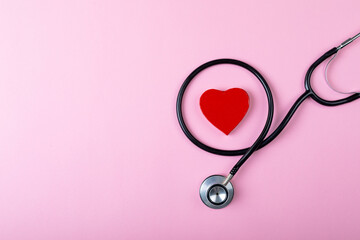 Overhead view of stethoscope and heart shaped decoration on pink background, copy space