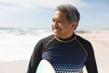 Retired senior smiles with surfboard on sunny beach