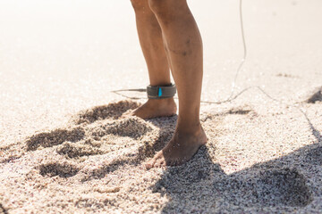 Low section of senior man with barefoot and surfboard leash on ankle at sunny beach