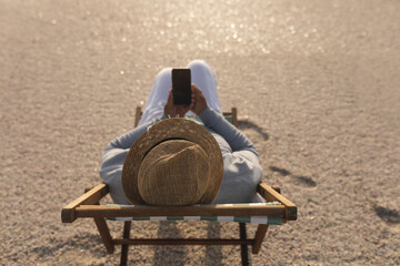 High angle view of senior woman using smartphone while sitting on folding chair at beach