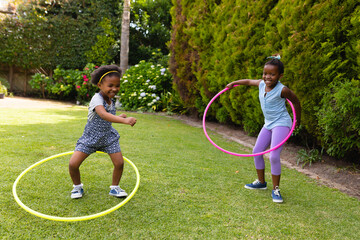 Full length of cheerful african american sisters enjoying with plastic hoops at garden