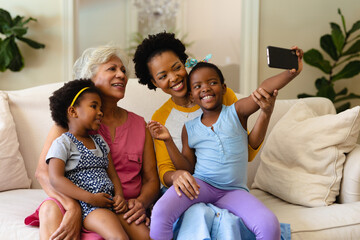 African american grandmother, mother and two granddaughters taking a selfie sitting on couch
