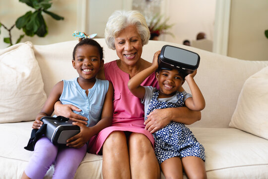 African american grandmother and her two granddaughters with vr headsets sitting on couch at home - Powered by Adobe