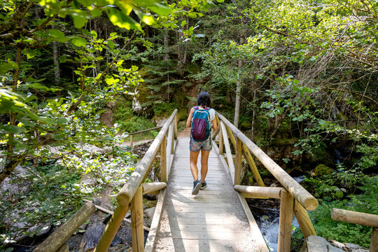 Woman hiking across wooden bridge in green forest trail