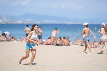 A woman runs on the beach while a crowd of people watch. The beach is crowded with people, some of whom are sunbathing