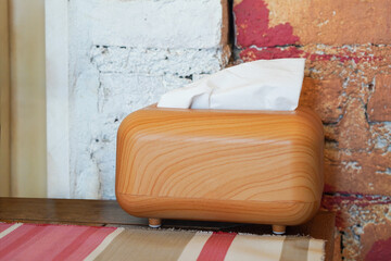 The tissues are in a rectangular wooden box, placed and colorful cloth on a wooden table, cement wall background