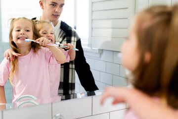 Teenage brother holding twin sisters while brushing their teeth in the bathroom