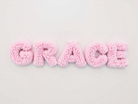 Pink fuzzy knitted letters spelling out the word GRACE on a white background