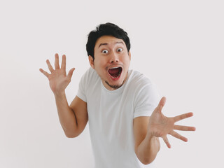 Asian man making excited expression with raised hands and wide eyes in white shirt and clean background