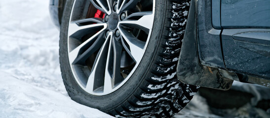 Low angle view of an automobile wheel with red brake caliper and deep tread pattern. Vehicle parked on a snowy road during a cold blizzard. Transportation and climate safety. Photo