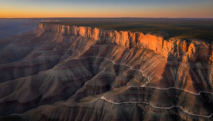 Aerial view of sunset over canyon landscape with rugged terrain and winding roads