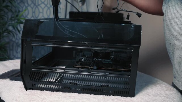 Connecting cables to motherboard during computer build process, close-up of male hand managing wires inside compact transparent case with CPU cooler already mounted
