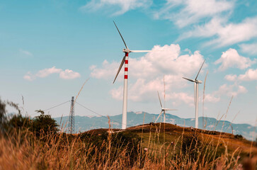 Wind turbines lined in a sunny mountain landscape, blending nature with clean energy.