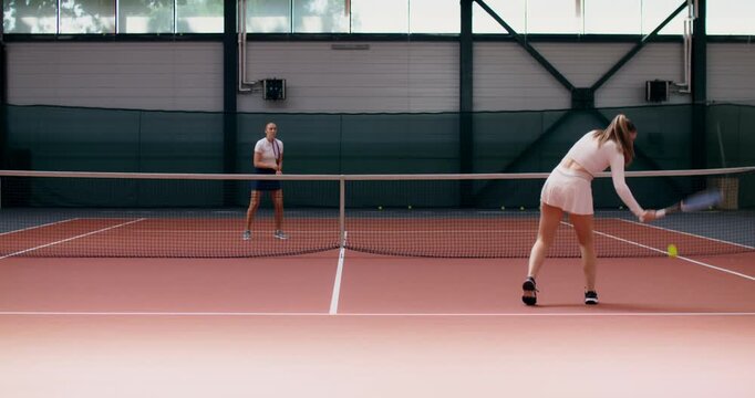 Two girls practicing on a tennis court with rackets in their hands. Two female tennis players play a training match on the court.